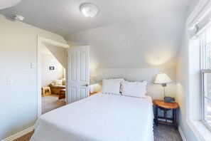 A bedroom with a large bed, a nightstand, a lamp, and a window.