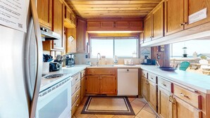 Cocina compacta con armarios de madera, refrigerador de acero inoxidable, lavavajillas y ventana que proporciona luz natural.