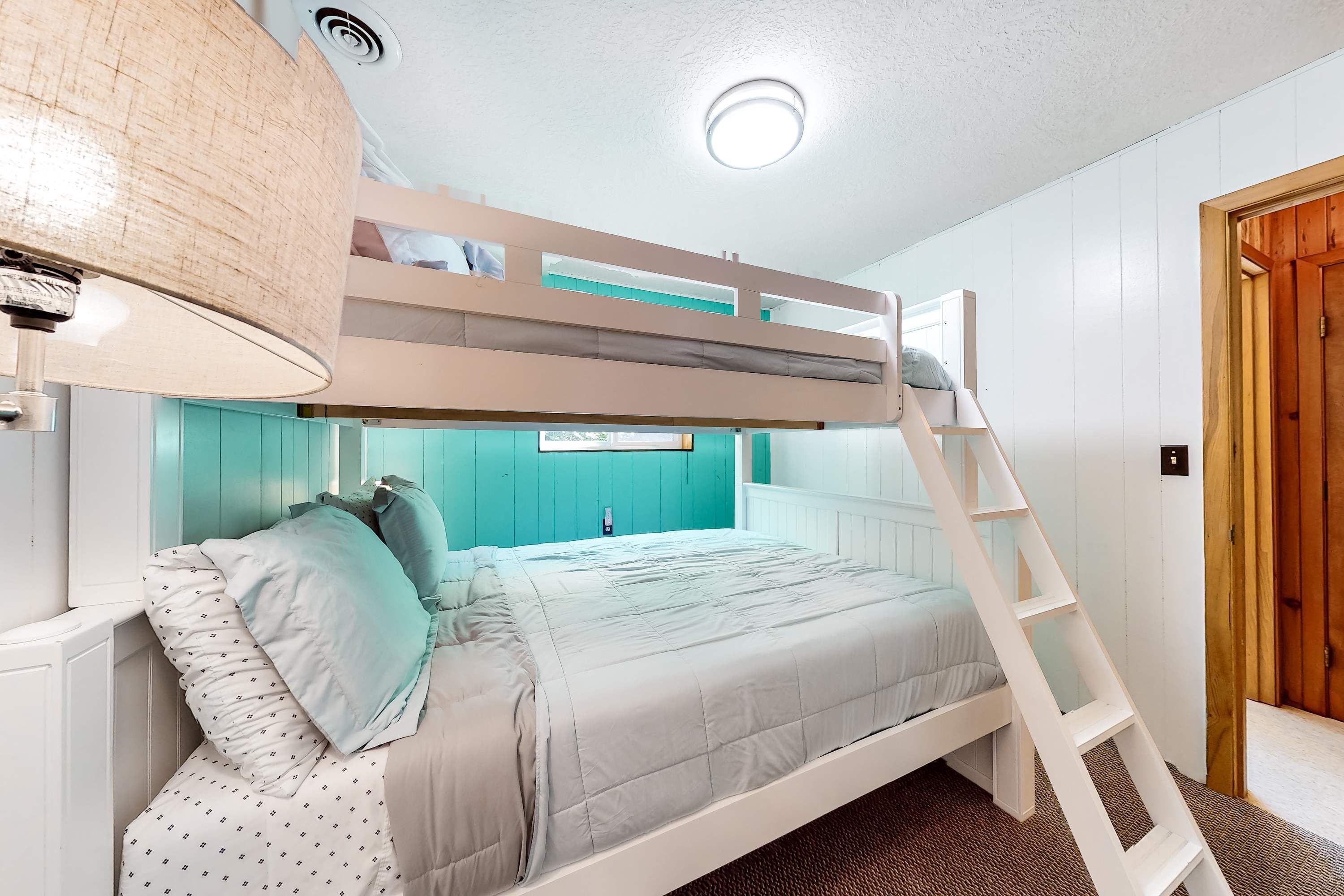 Un lit superposé avec une échelle, une fenêtre avec des murs de couleur turquoise et une porte en bois.