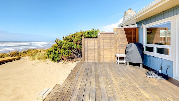 Un ponte di legno con vista sull'oceano, un barbecue coperto e un tavolino.