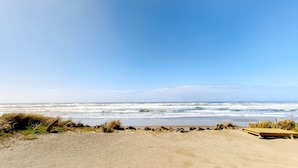 Una spiaggia con una passerella in legno, una battigia sabbiosa e onde oceaniche.