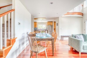 Un comedor amplio con una mesa y sillas de madera, una cocina al fondo y una escalera a la izquierda.