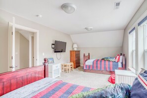 A bedroom with two beds, a desk, a chair, a television, and a window.