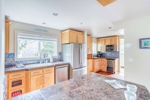 A modern kitchen with wooden cabinets, a stainless steel refrigerator, and a granite countertop. - Spacious coastal retreat | 3-min walk to beach | Decks & mountain views (Rockaway Beach)