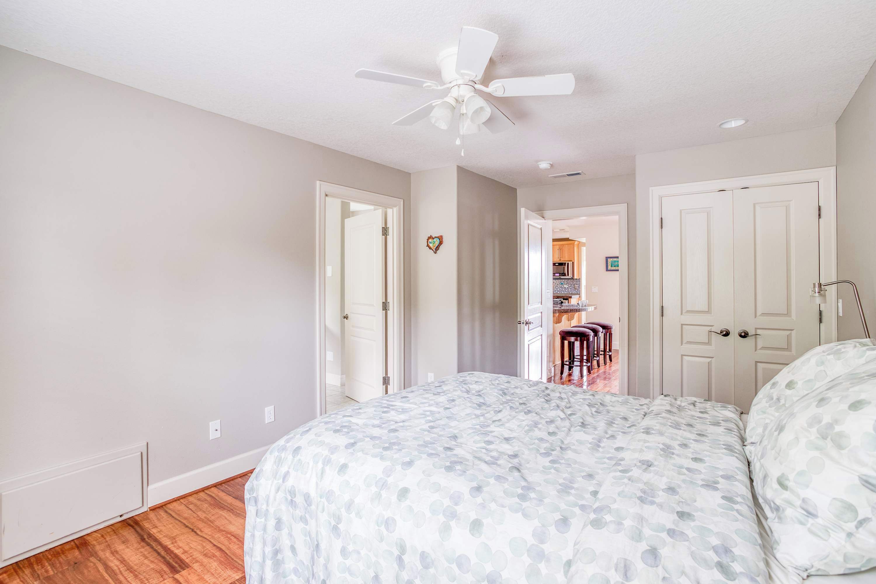 A bedroom with a bed, a ceiling fan, and a view into the kitchen area.