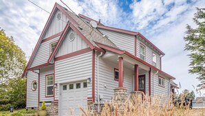 A two-story house with a garage, a stone foundation, and a red and white exterior. - Spacious coastal retreat | 3-min walk to beach | Decks & mountain views (Rockaway Beach)