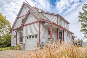 A two-story house with a garage, a stone foundation, and a red and white exterior. - Spacious coastal retreat | 3-min walk to beach | Decks & mountain views (Rockaway Beach)