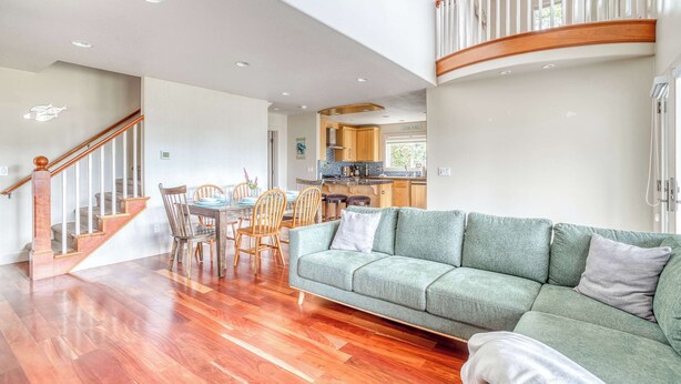 A spacious living area with a wooden staircase, a dining table with chairs, and a green sofa. - Spacious coastal retreat | 3-min walk to beach | Decks & mountain views (Rockaway Beach)