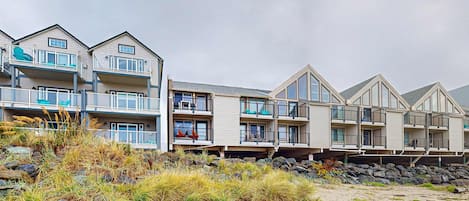 A beachfront hotel with multiple balconies, a sandy beach, and a rocky shoreline.