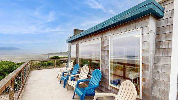 A covered outdoor seating area with Adirondack chairs, a wooden deck, and a view of the beach. - Oceanfront home with great views high speed WiFi and direct beach access (Rockaway Beach)