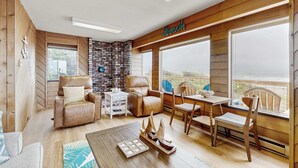 A cozy room with a fireplace, leather chairs, a wooden table, and a view of the beach. - Oceanfront home with great views high speed WiFi and direct beach access (Rockaway Beach)