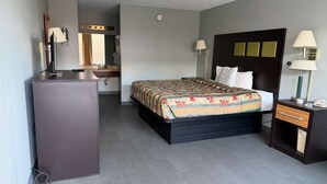 A hotel room with a bed, a desk, a chair, a mirror, and a wardrobe.