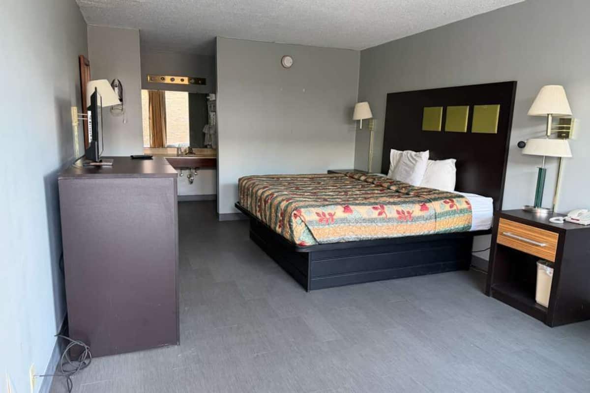 A hotel room with a bed, a desk, a chair, a mirror, and a wardrobe.