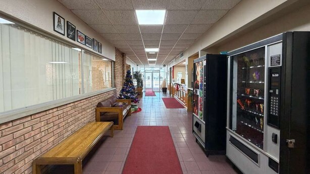 A corridor with a brick wall, wooden benches, a Christmas tree, vending machines, and a red carpet.
