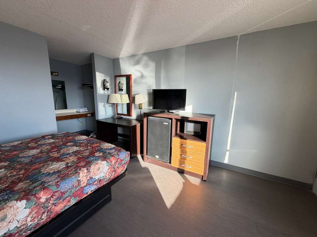 A bedroom with a bed, a TV, a dresser, and a mirror.