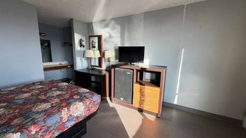 A bedroom with a bed, a TV, a dresser, and a mirror.