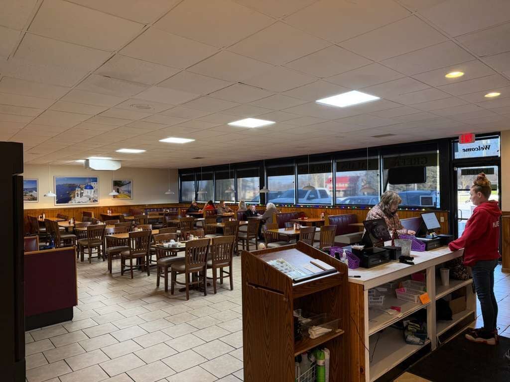 En rymlig restaurang med många bord och avskilda sittplatser, en bardisk med en meny och utsikt över gatan genom stora fönster.