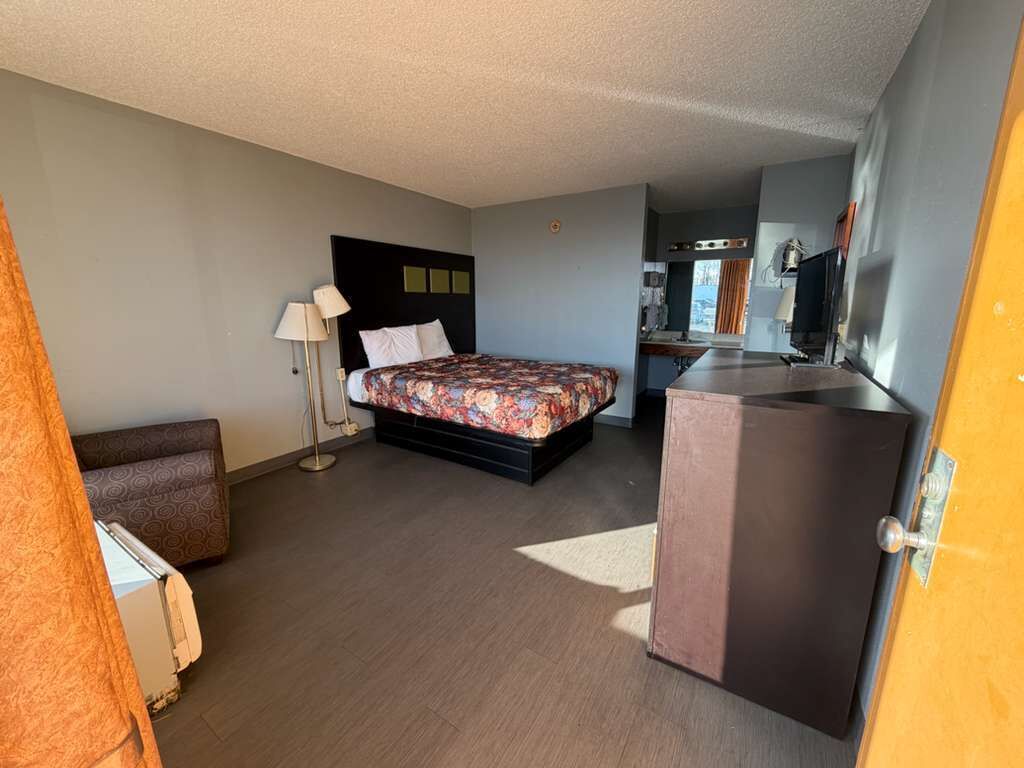 Une chambre d’hôtel de taille réduite, comprenant un lit, un petit canapé, un bureau et une kitchenette.