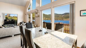 Un soggiorno moderno con una grande TV, un tavolo da pranzo e vista su un lago e montagne.