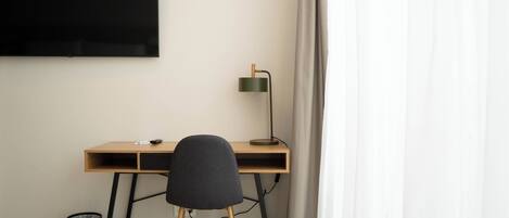A minimalist workspace with a wooden desk, a black chair, a floor lamp, and a black trash can.