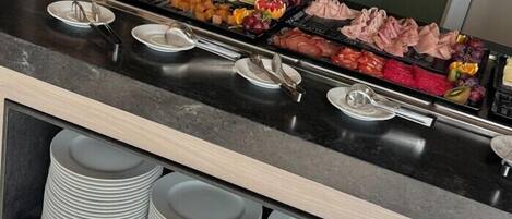 Ein reichhaltiges Buffet mit verschiedenen Speisen und gestapelten weißen Tellern.