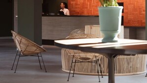 Un espace d’accueil avec un mur en bois, une réceptionniste, un vase bleu clair orné de fleurs et des meubles modernes.