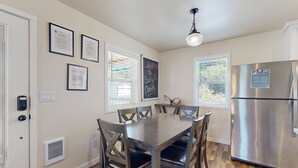 A modern kitchen with a stainless steel refrigerator, a dining table with chairs, and framed certificates on the wall. - Modern Beach Cottage with a covered patio fire pit grill and easy beach access (Rockaway Beach)