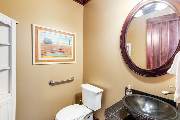 Een badkamer met een beige wand, een wanddecoratie van een strandlandschap, een wit toilet, een ronde spiegel en een zwart wastafel.