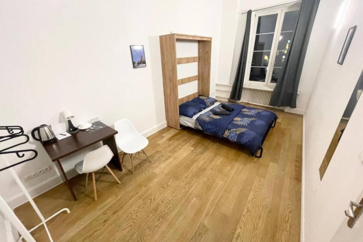 A small, well-lit room with a bed, a desk, and a chair.