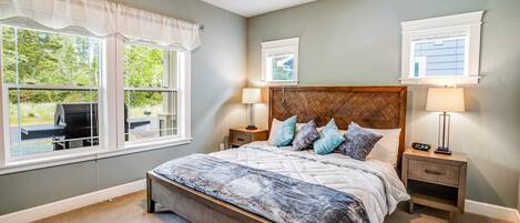 A bedroom with a large bed, two bedside tables with lamps, a headboard, and two windows with curtains.