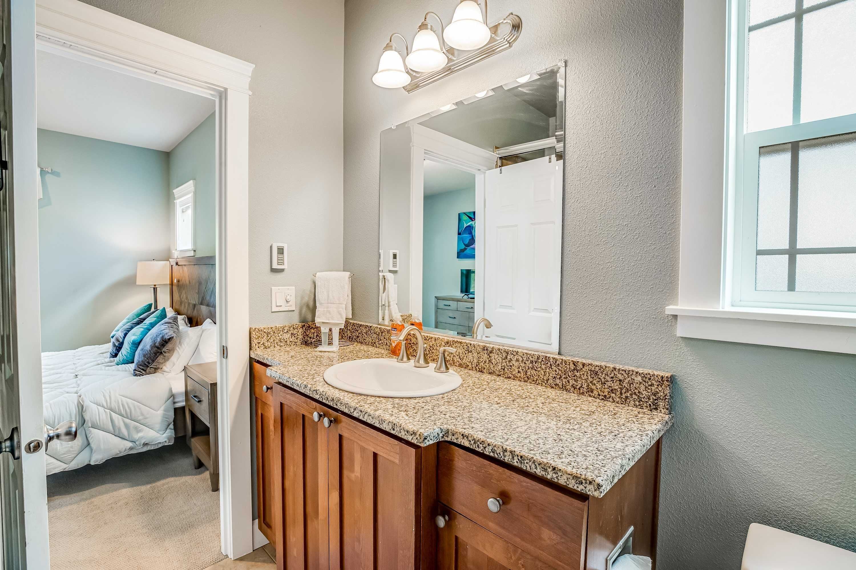 A bathroom with a granite countertop sink, wooden vanity, and a large mirror.