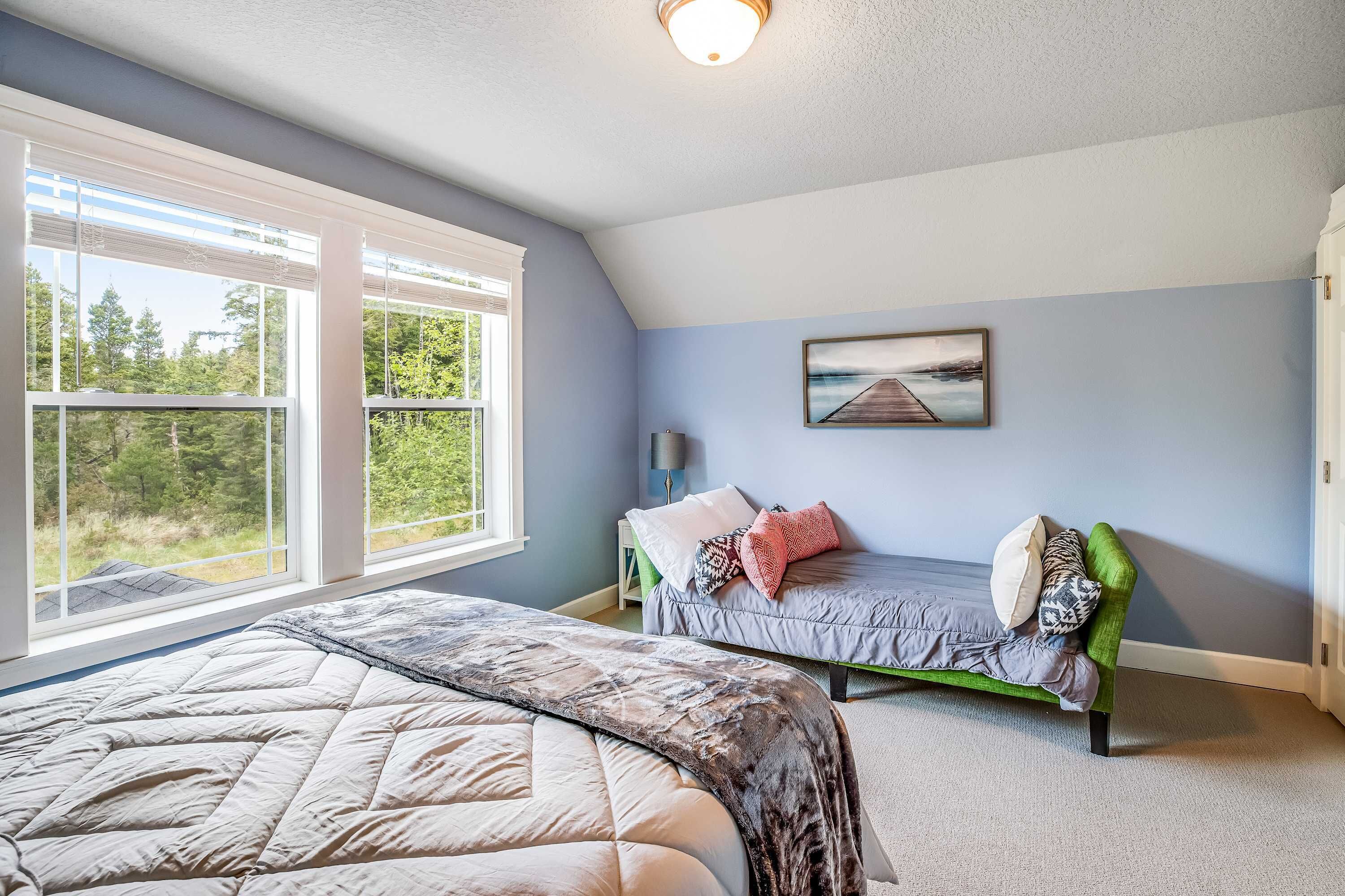 A bedroom with a large window, a bed, a green sofa, and a painting on the wall.