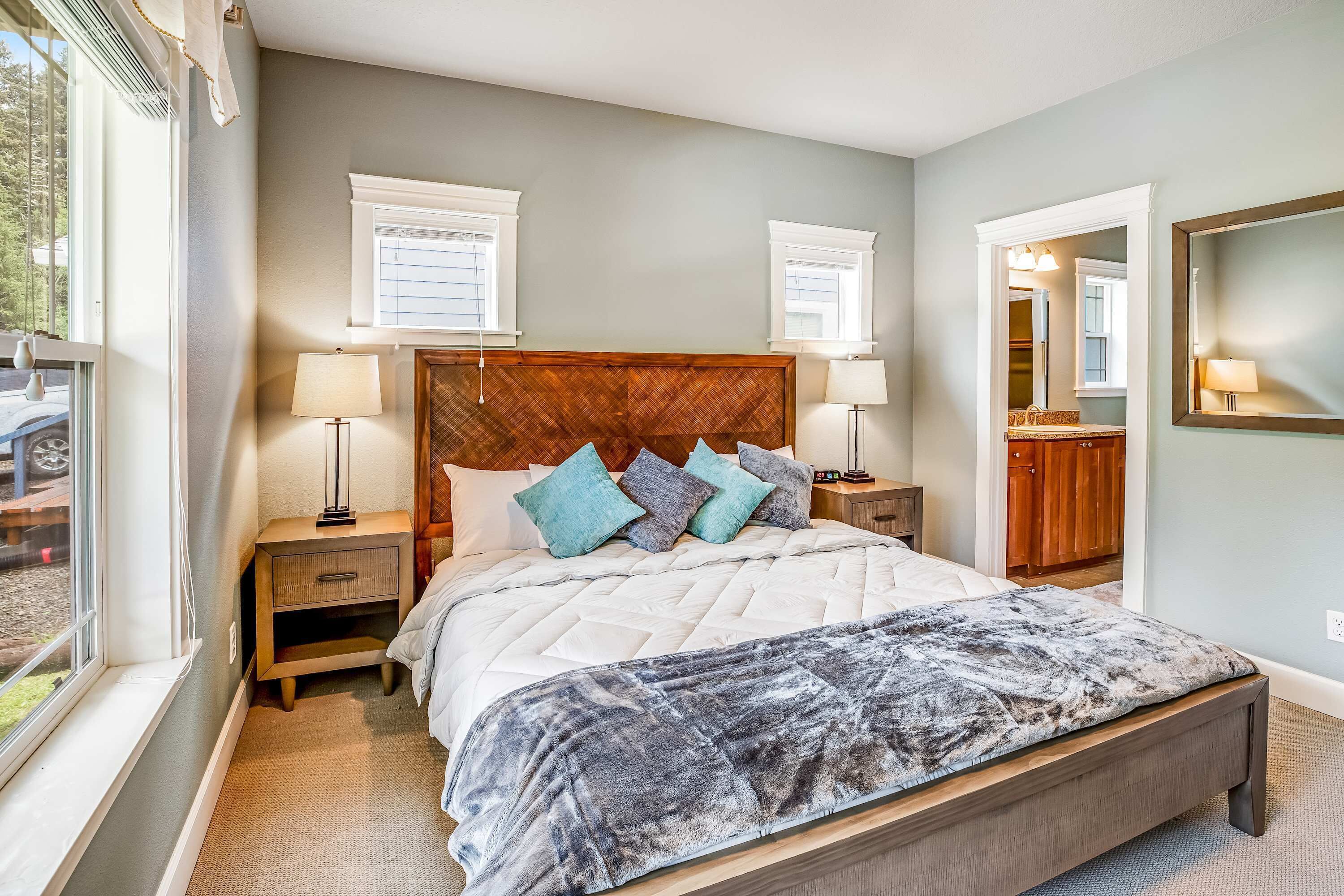 A bedroom with a large bed, two bedside tables, a headboard, and a window with blinds.