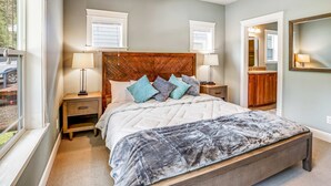 A bedroom with a large bed, two bedside tables, a headboard, and a window with blinds.