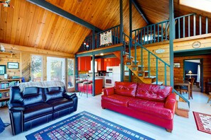 A spacious living area with a high ceiling, a red leather sofa, a black leather sofa, and a patterned rug.