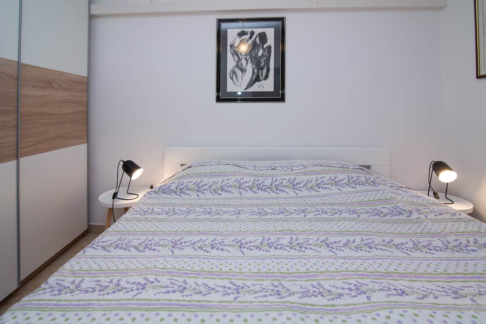A neatly made bed with a patterned bedspread, two bedside lamps, and a framed artwork on the wall.
