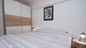 Un dormitorio con cama, mesita de noche, armario y una obra de arte enmarcada en la pared.