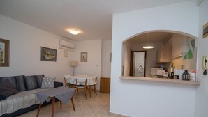 Una sala de estar con sofá, una mesa de comedor y una zona de cocina con fregadero y armarios.