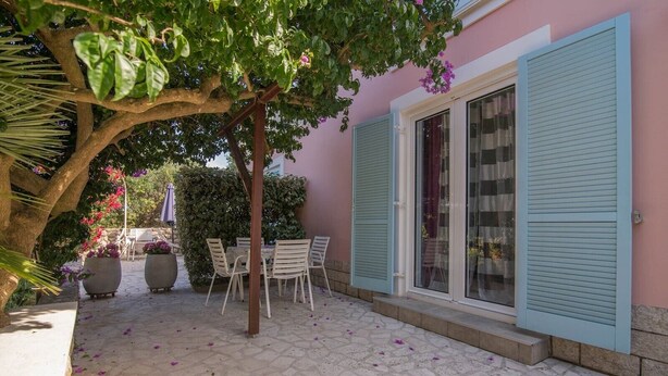 Un patio con una mesa y sillas, un árbol y un edificio con contraventanas azules.