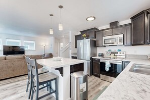 A modern kitchen with dark cabinets, stainless steel appliances, and a marble countertop. - Open concept Home with Deck Fire pit WIFI and Near Trails and Beach (Rockaway Beach)
