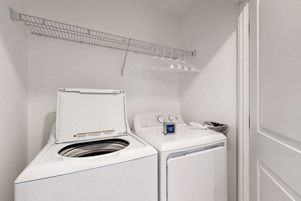 A compact laundry area with a front-loading washer and dryer, a drying rack, and a small trash bin. - Open concept Home with Deck Fire pit WIFI and Near Trails and Beach (Rockaway Beach)