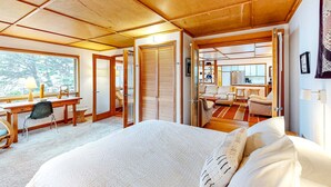 A spacious bedroom with a large bed, a desk, and a chair. There is a wardrobe and a bathroom visible in the background. - Delightful dog friendly home with bay views private hot tub and sauna (Rockaway Beach)