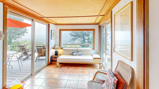 A room with a sliding glass door leading to an outdoor area, a bed, a wicker chair, and a table with a lamp. - Delightful dog friendly home with bay views private hot tub and sauna (Rockaway Beach)