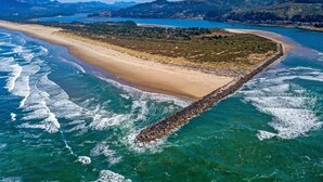 An aerial view of a coastal area with a sandy beach, a rocky breakwater, and a backdrop of hills and a body of water. - Delightful dog friendly home with bay views private hot tub and sauna (Rockaway Beach)