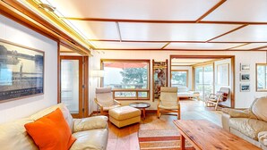 A spacious living room with a large window, leather sofas, wooden flooring, and a view of the outdoors. - Delightful dog friendly home with bay views private hot tub and sauna (Rockaway Beach)