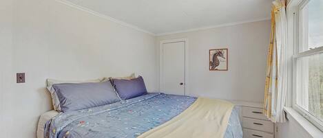 Een slaapkamer met een bed, nachtkastje, raam met gordijnen, een deur en een plafondlamp.