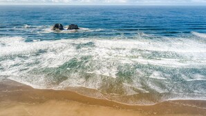 Ein Strand mit ankommenden Wellen und einer Felsformation im Wasser.