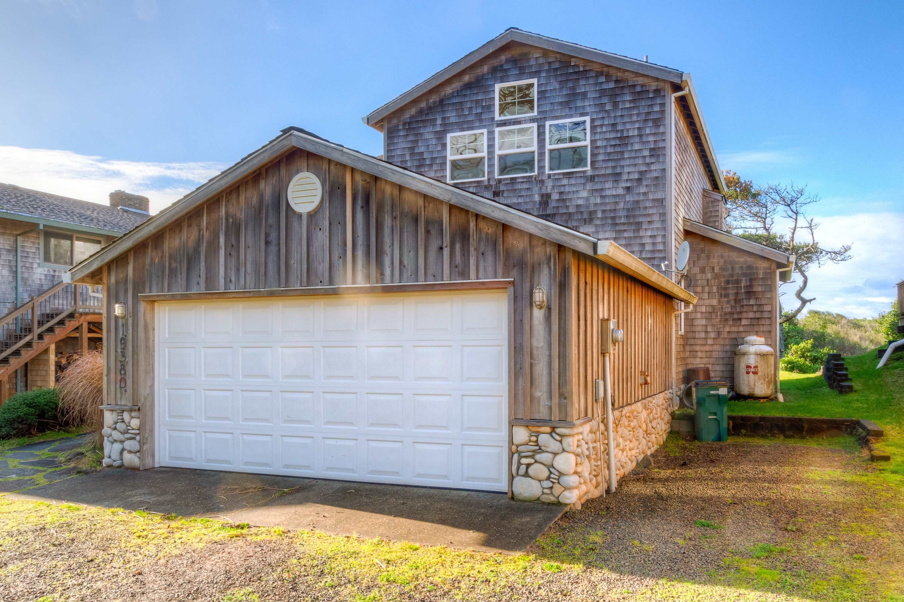 Une maison à deux étages avec un garage, des fondations en pierre et un revêtement extérieur en bois.