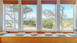 Ein Zimmer mit vier Fenstern, jedes mit Blick auf den Strand und Bäume.