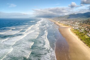 An aerial view of a beach with waves, a town, and mountains in the background. - Beachfront home with private beach access fireplace washer dryer yard deck (Rockaway Beach)